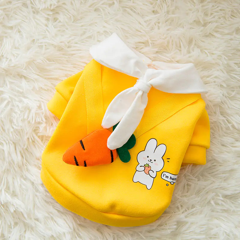Yellow pet hoodie with bunny ears and carrot design on a fluffy white surface